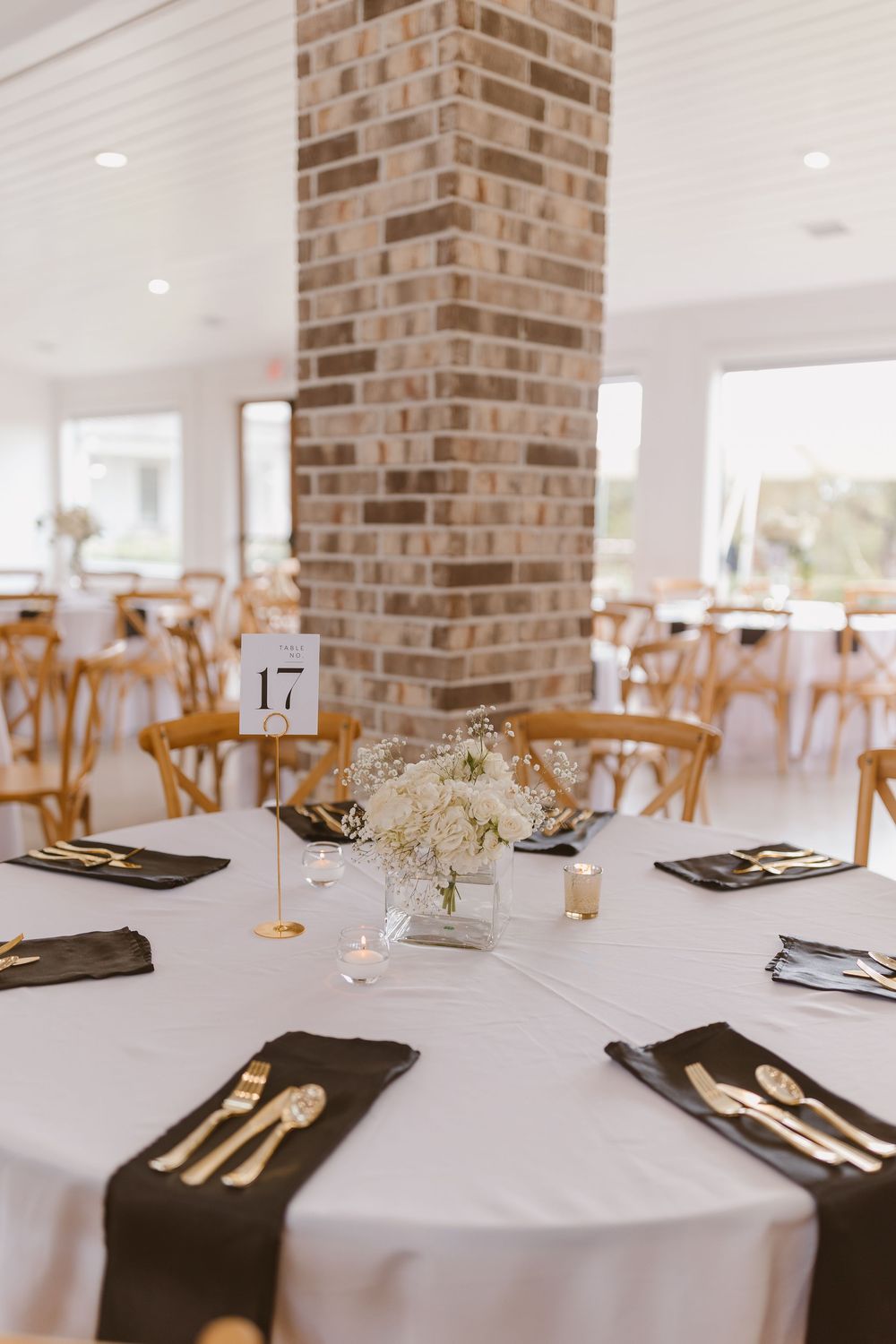 Modern wedding table settings featuring white linens, black napkins, and gold accents against exposed brick walls.