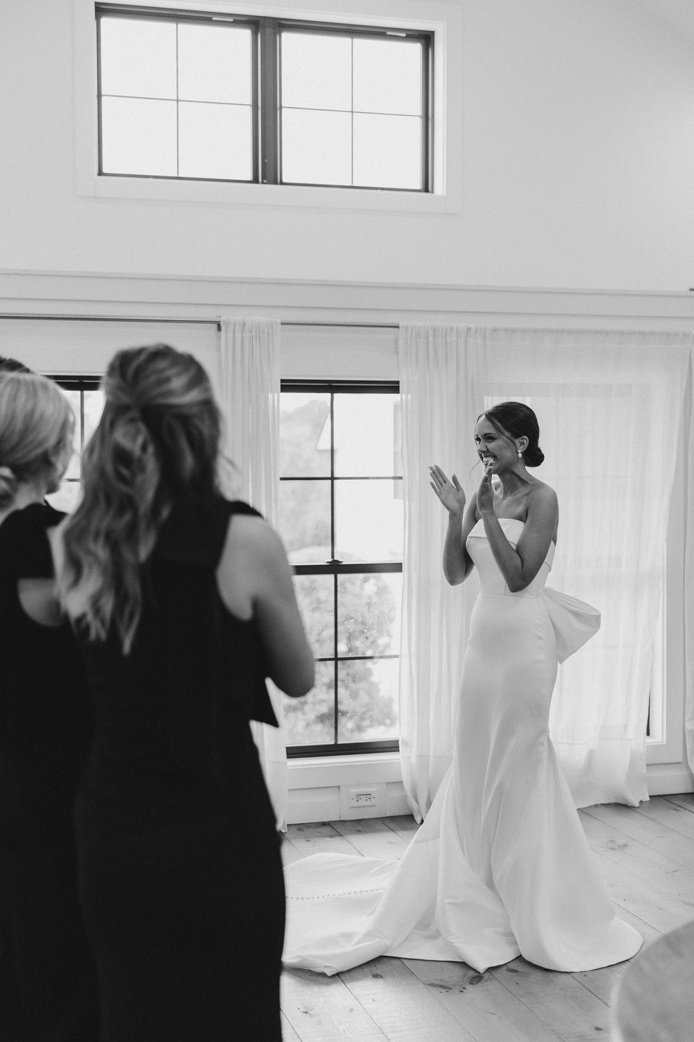 Black and white emotional first look moment in a bright, window-lit room with white curtains.