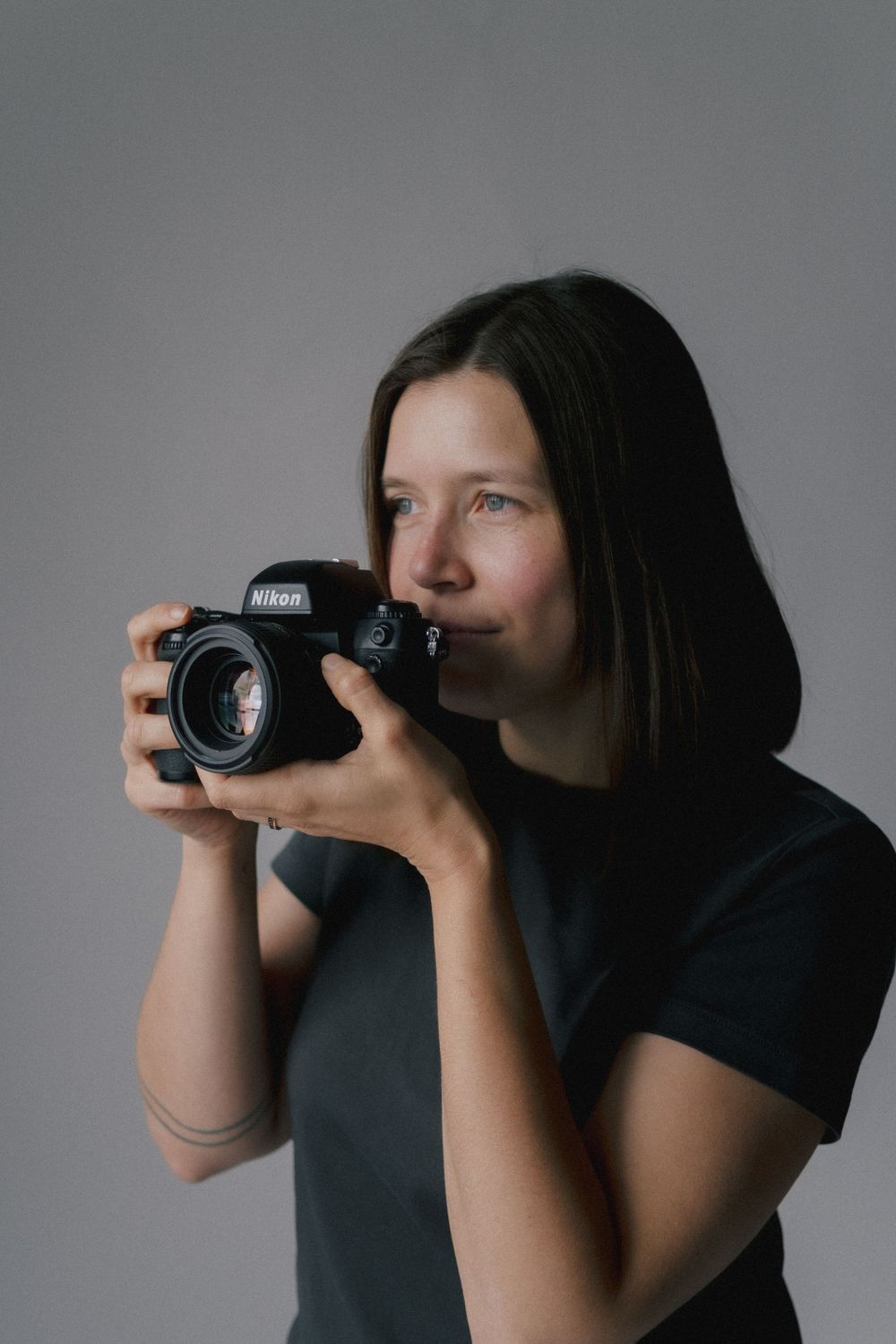 A photographer in dark clothing demonstrates four different camera holding positions while taking photos against a gray background.