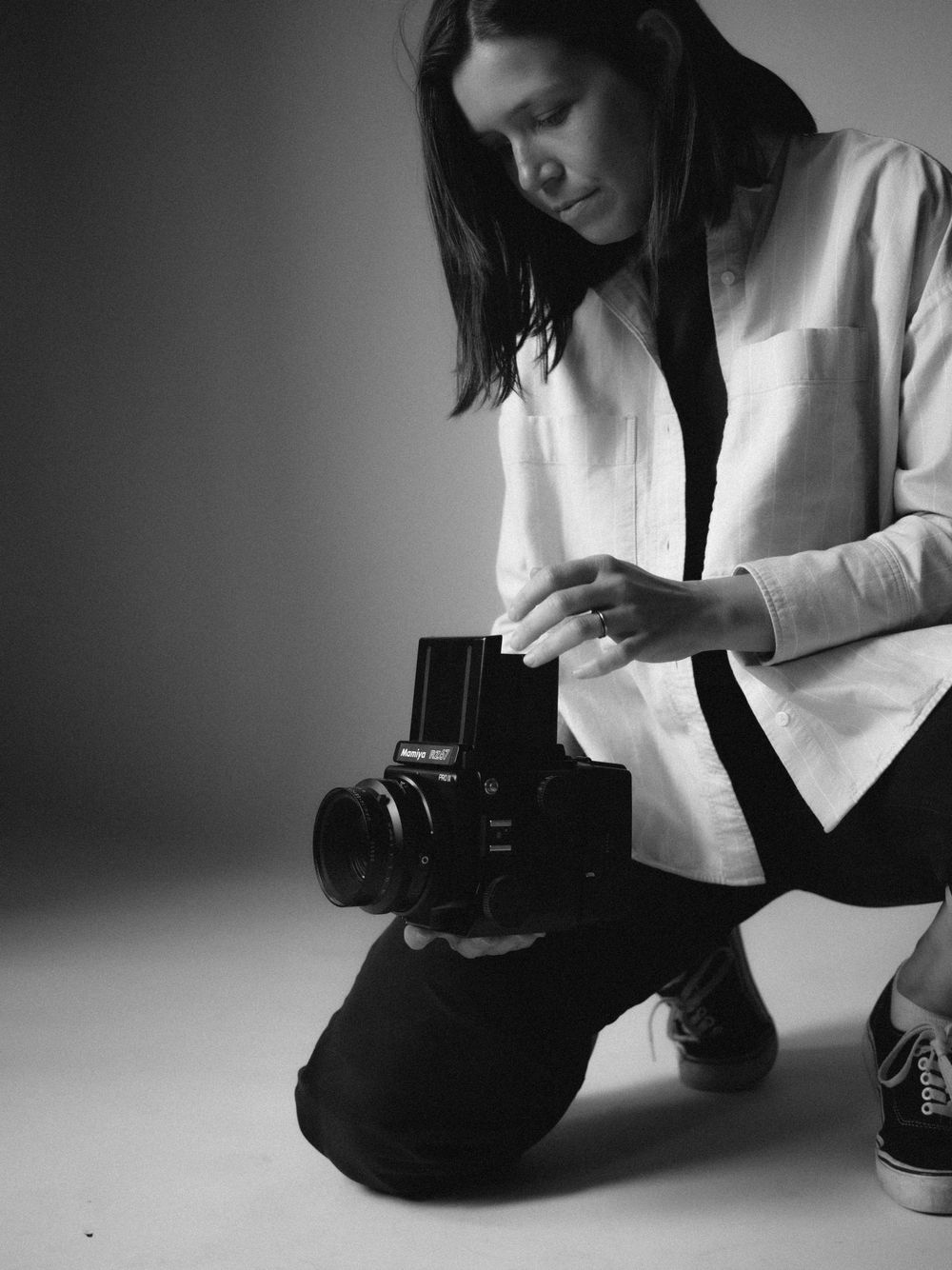A photographer in a white jacket and black pants kneels down while examining a medium format camera.