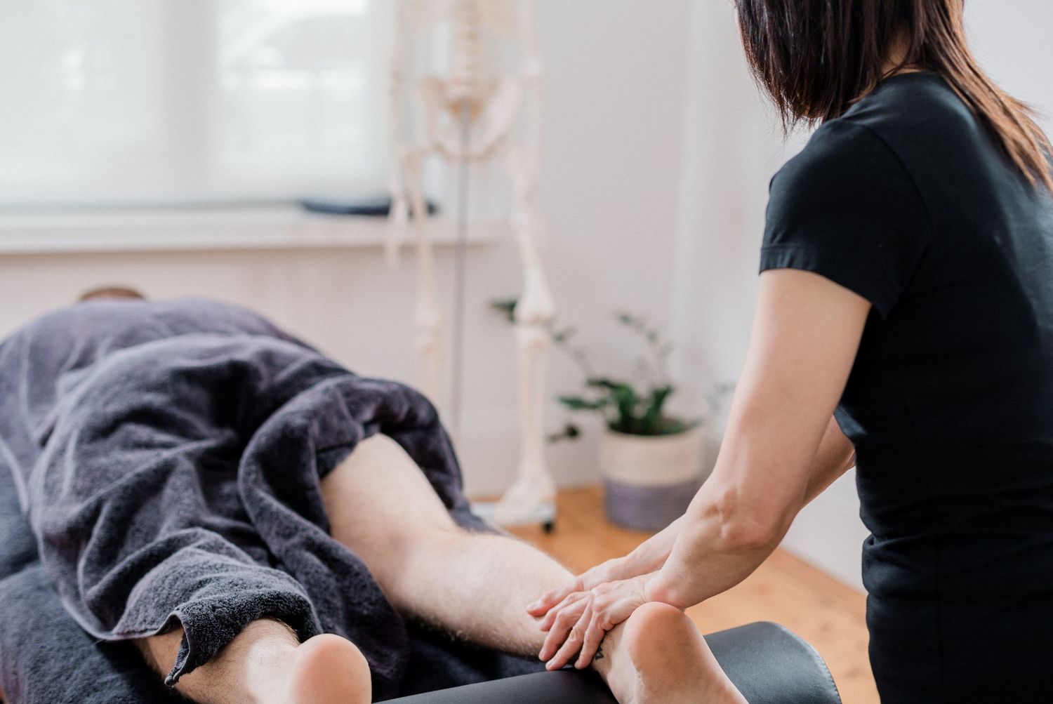 Massage therapist providing therapeutic treatment on gray massage table in clinical setting.