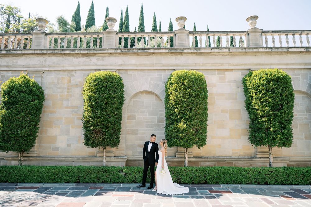 Wedding couple photographed against formal garden wall with trimmed topiary and cypress trees.