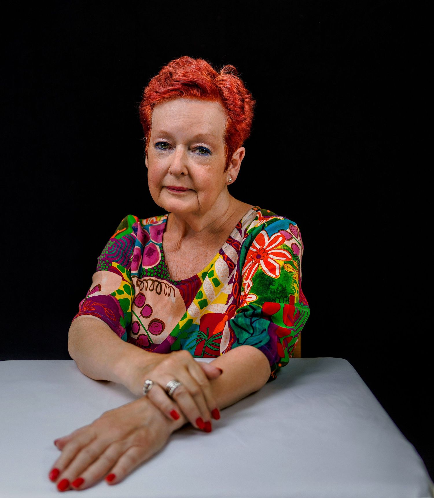 A person in a vibrant floral print top poses against a black background in a series of expressive portraits.