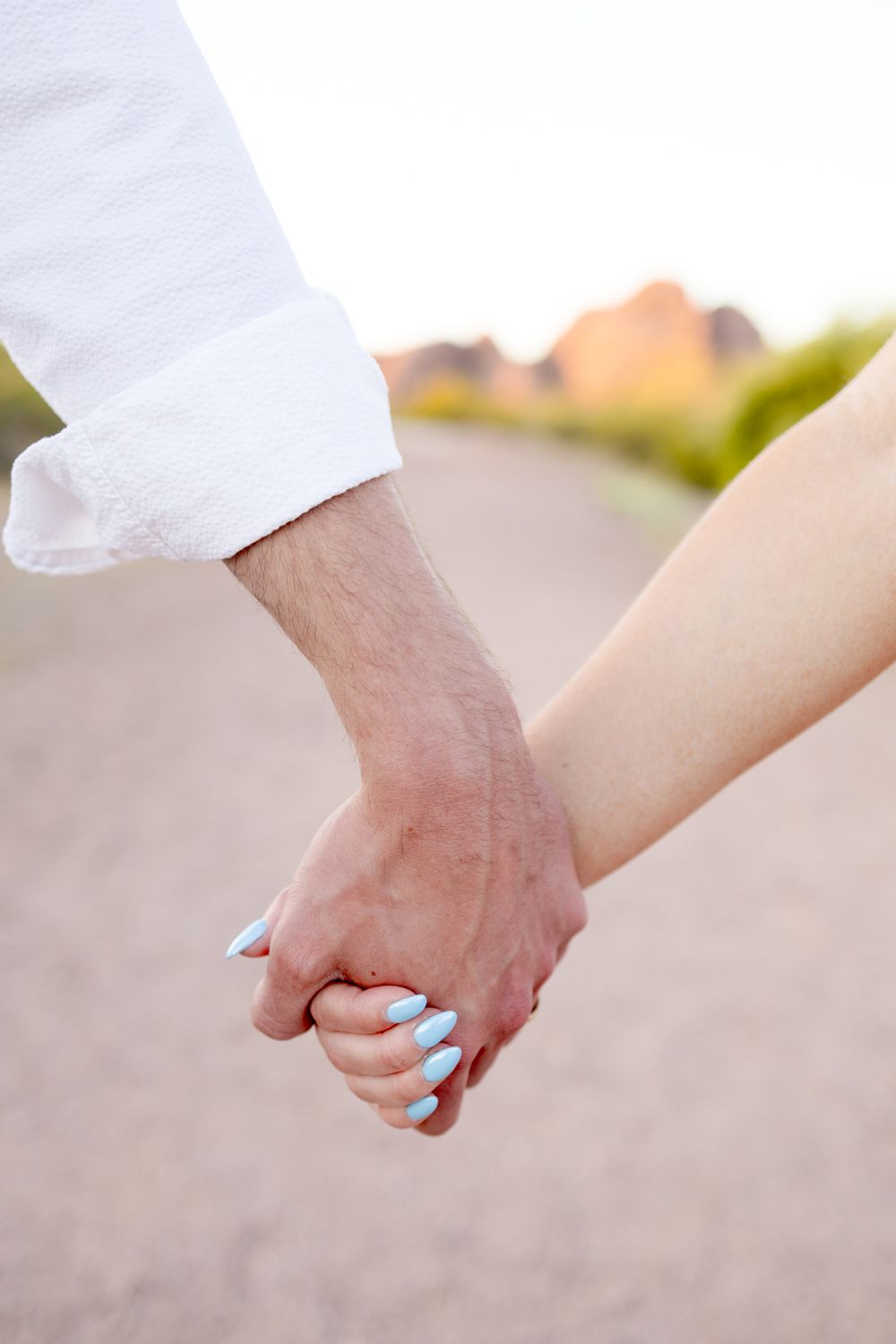 Close-up of two people holding hands romantically outdoors, with one person wearing light blue nail polish.