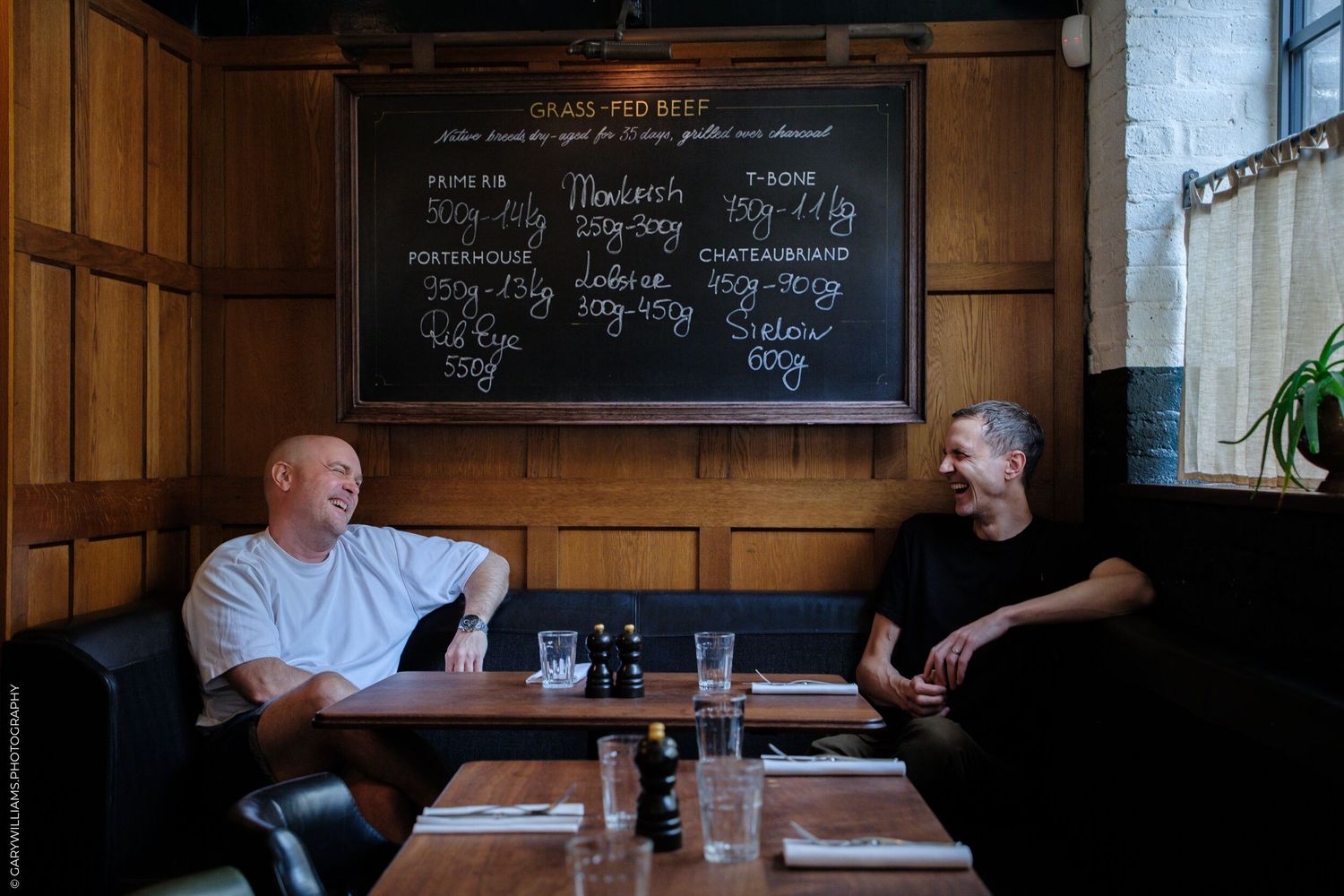 Diners seated at wooden tables inside a rustic restaurant with chalkboard menus on wood-paneled walls.