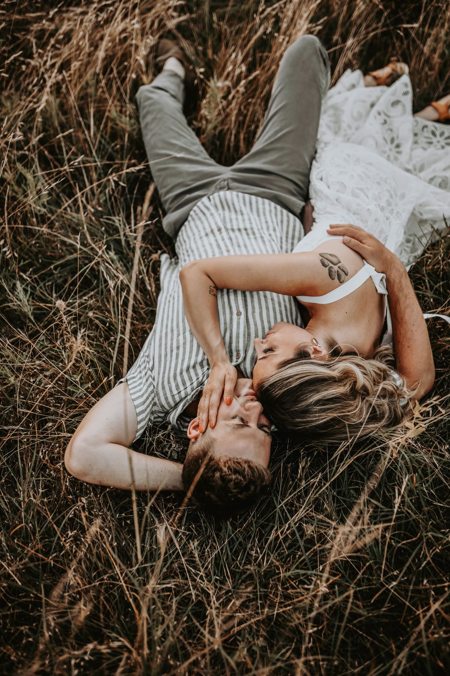 Sunset light beaming behind a couple sharing a forehead kiss in golden grass as they romantically cuddle in the grass