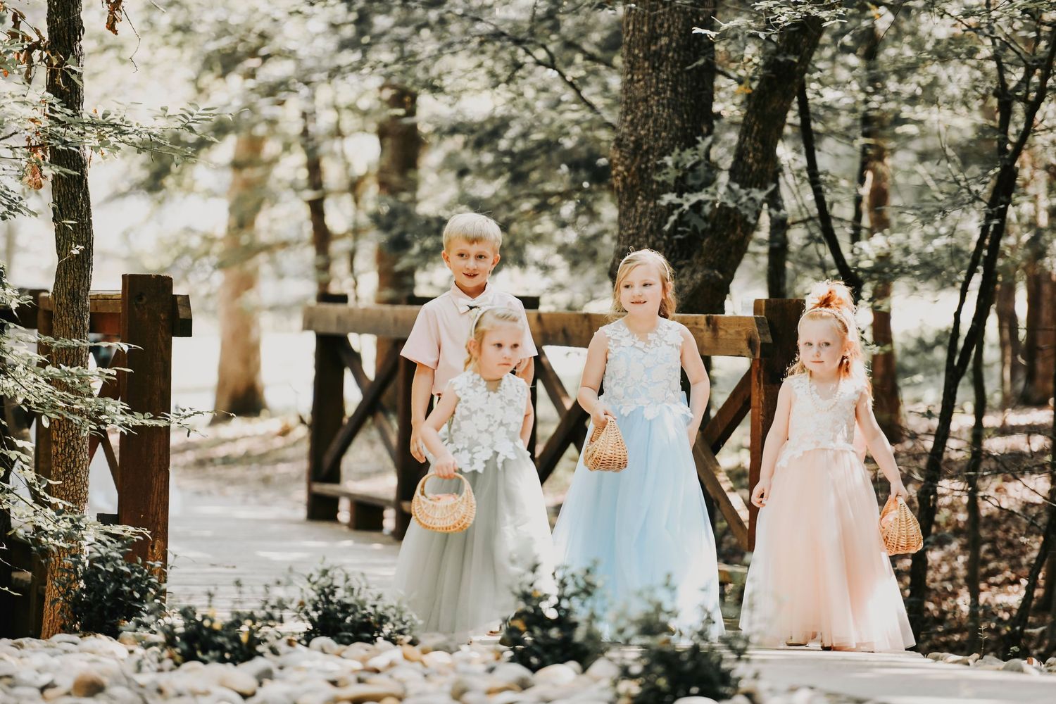 Little girls in flower crowns giggling as they walk down a rustic bridge