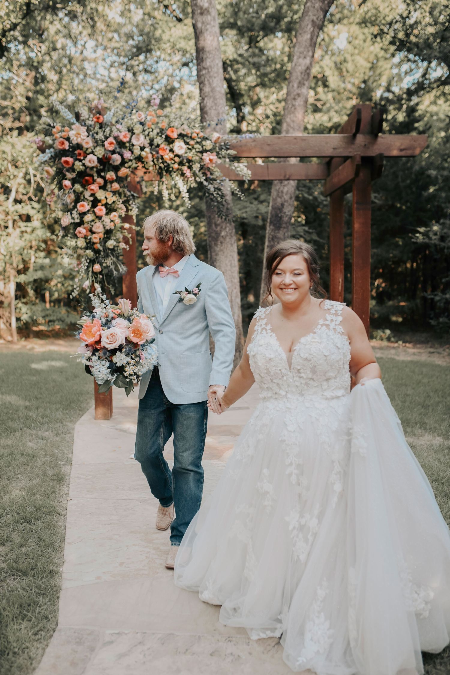 Bride and groom holding hands under a rustic wooden arbor adorned with spring blooms