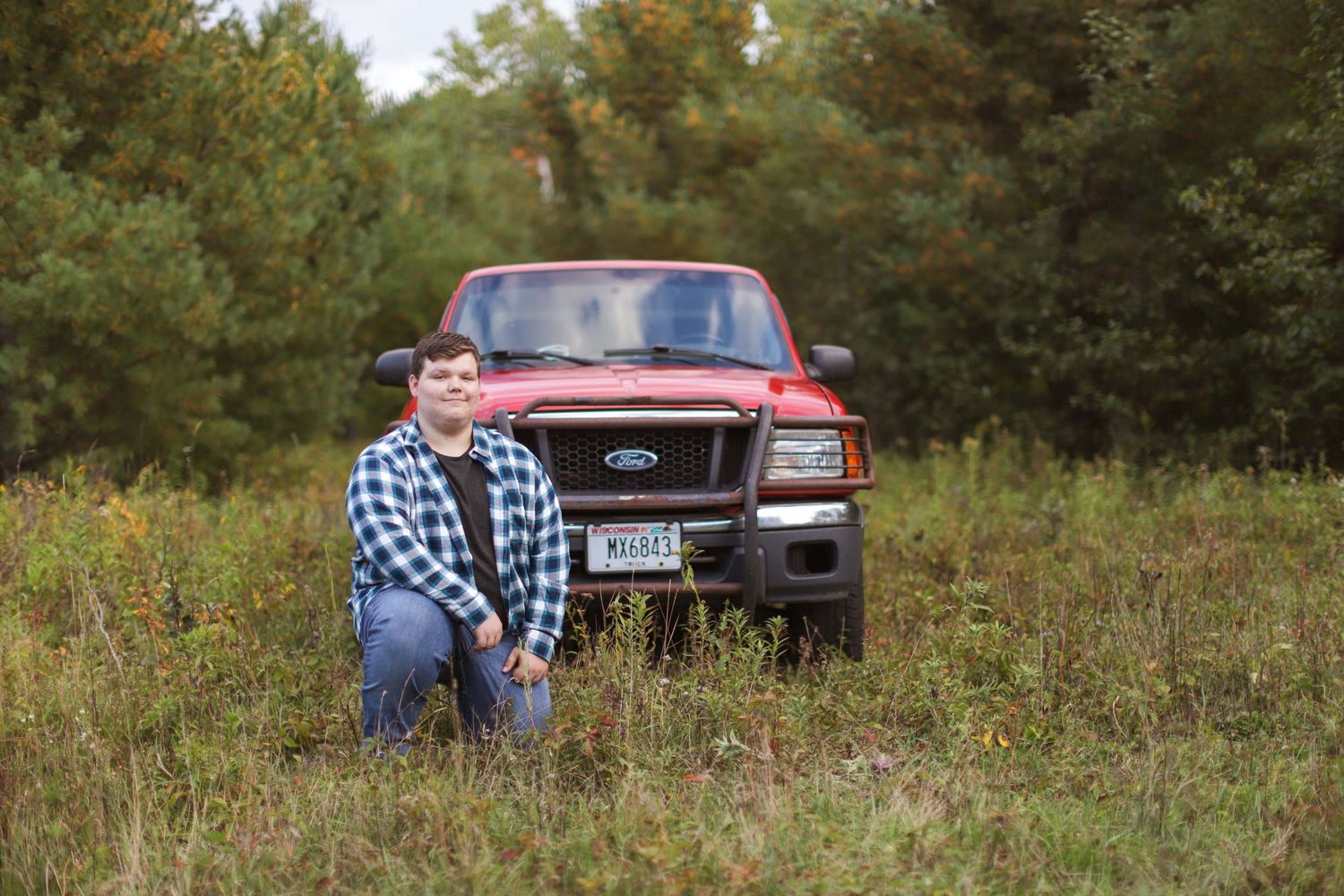 Red Ford pickup truck parked in a grassy field with trees in the background.