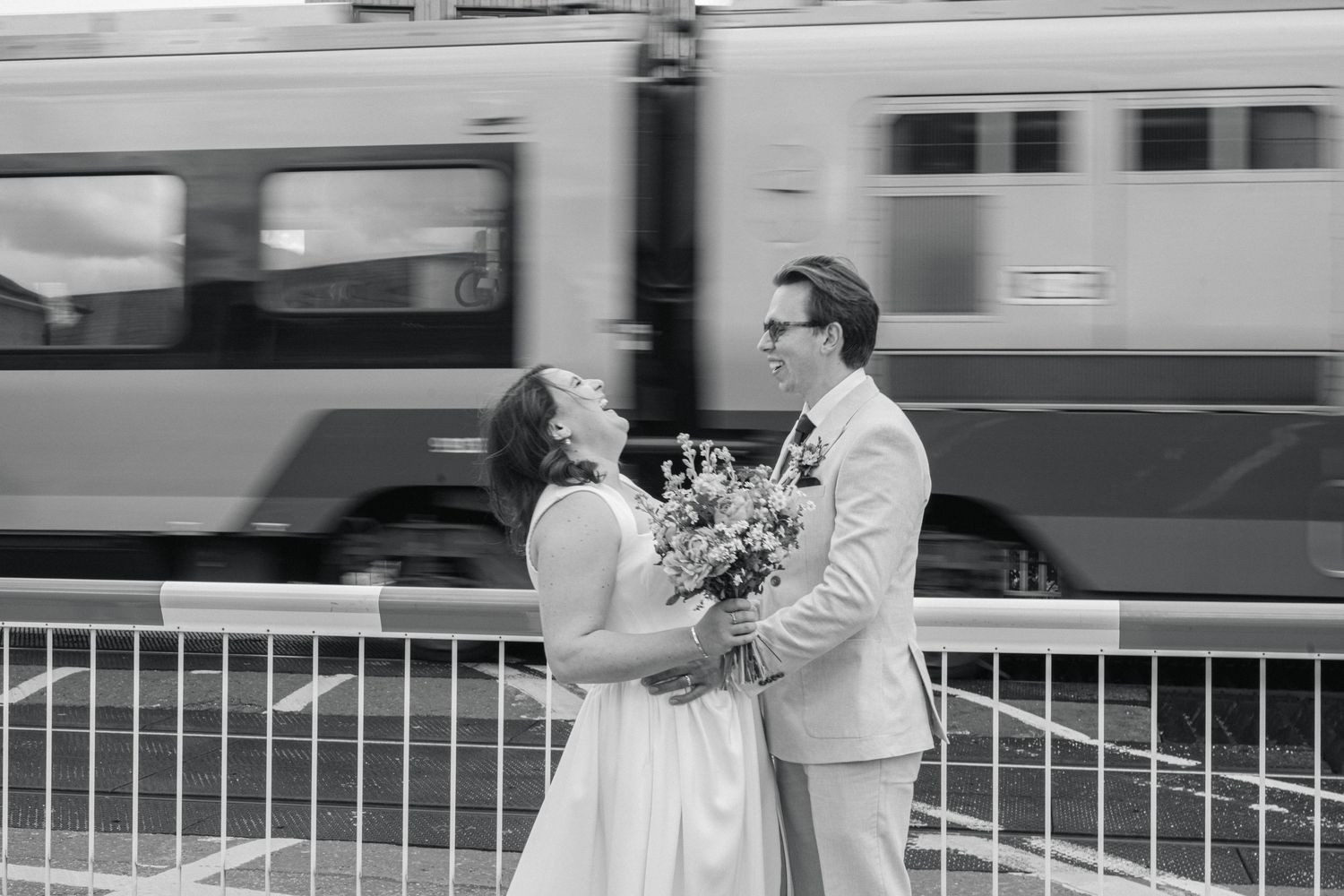 A couple shares a romantic moment on a train platform with a passing train in the background.