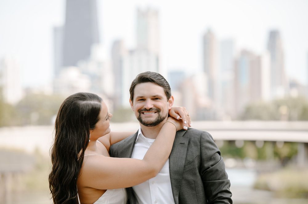 A couple laughs together during their engagement photoshoot with the Chicago skyline visible in the background.