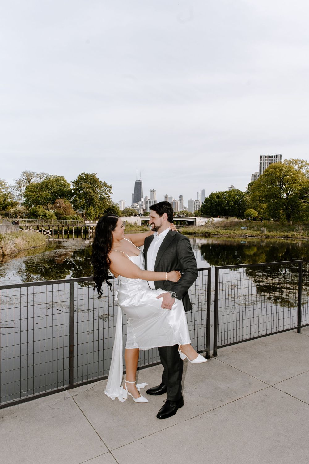 A romantic wedding photo sequence of a couple dipping and embracing on a riverside walkway overlooking the city skyline.