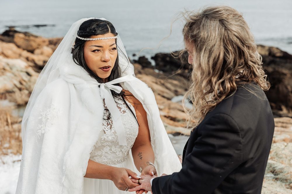 An intimate wedding ceremony unfolds against a dramatic rocky coastline backdrop on an overcast day.