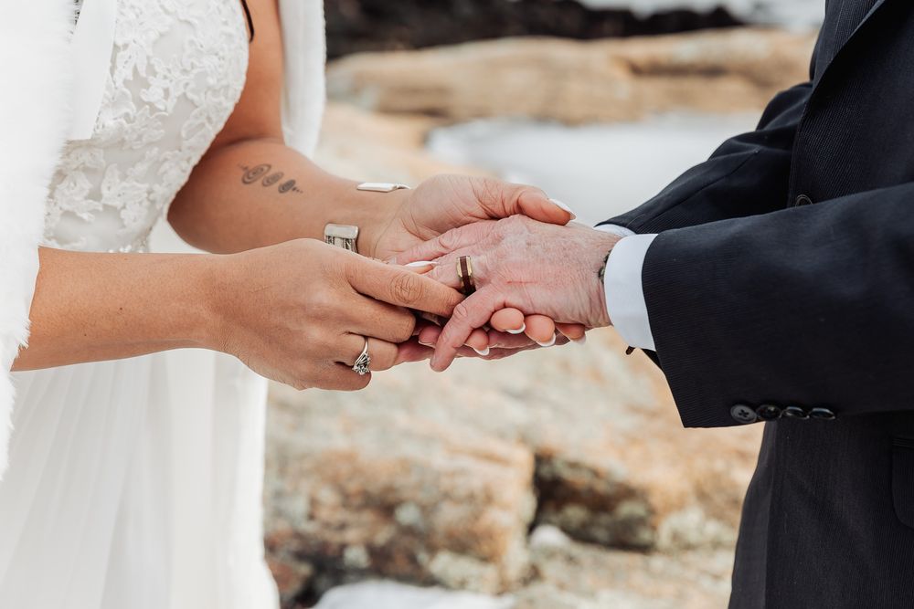 Close-up of hands exchanging wedding rings during an outdoor beach ceremony.