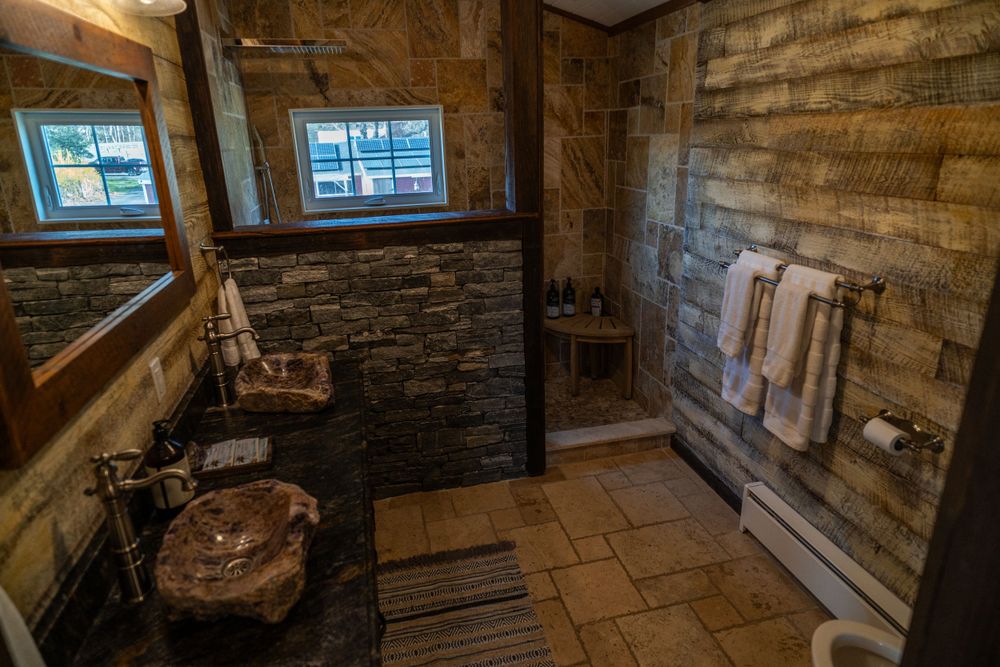 Bathroom with a stone half wall shower, amethyst sinks, and elegant wooden detailing for a luxurious rustic feel.