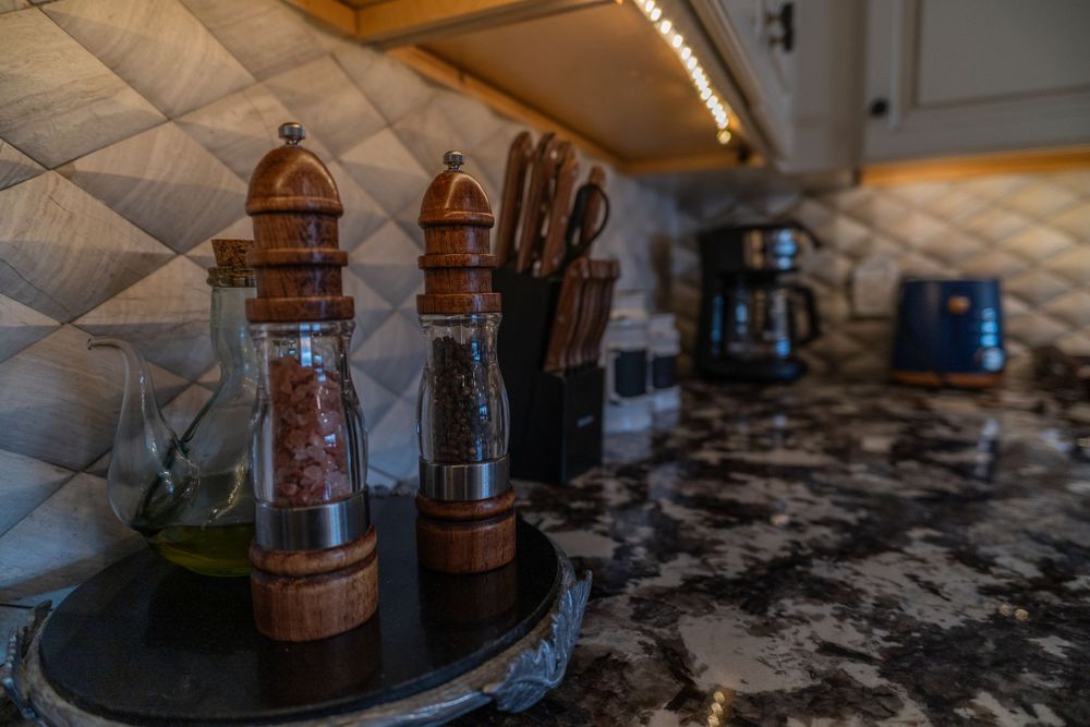 Close-up of kitchen counter with wooden and glass salt and pepper grinders, knives, coffee machine, and toaster in the background.