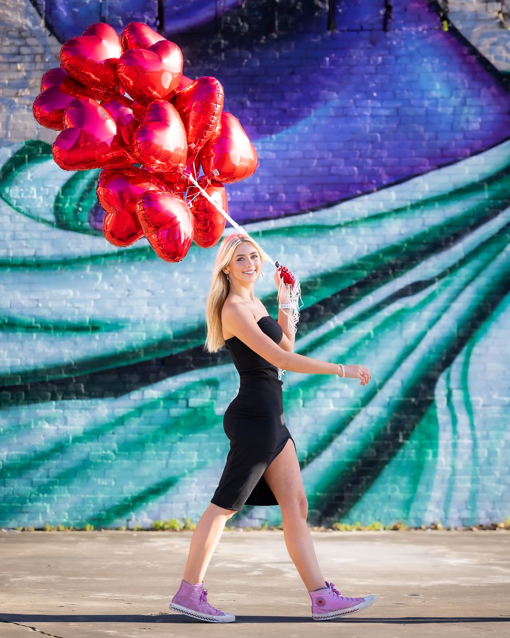 Perrysburg high school senior walking with red balloons with a bright mural as a background