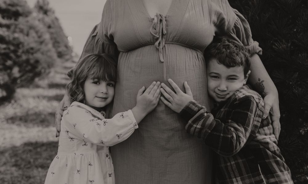 A black and white photograph showing children hugging a pregnant belly.
