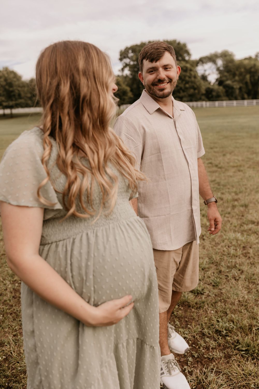Expectant couple sharing a tender moment in casual attire outdoors.