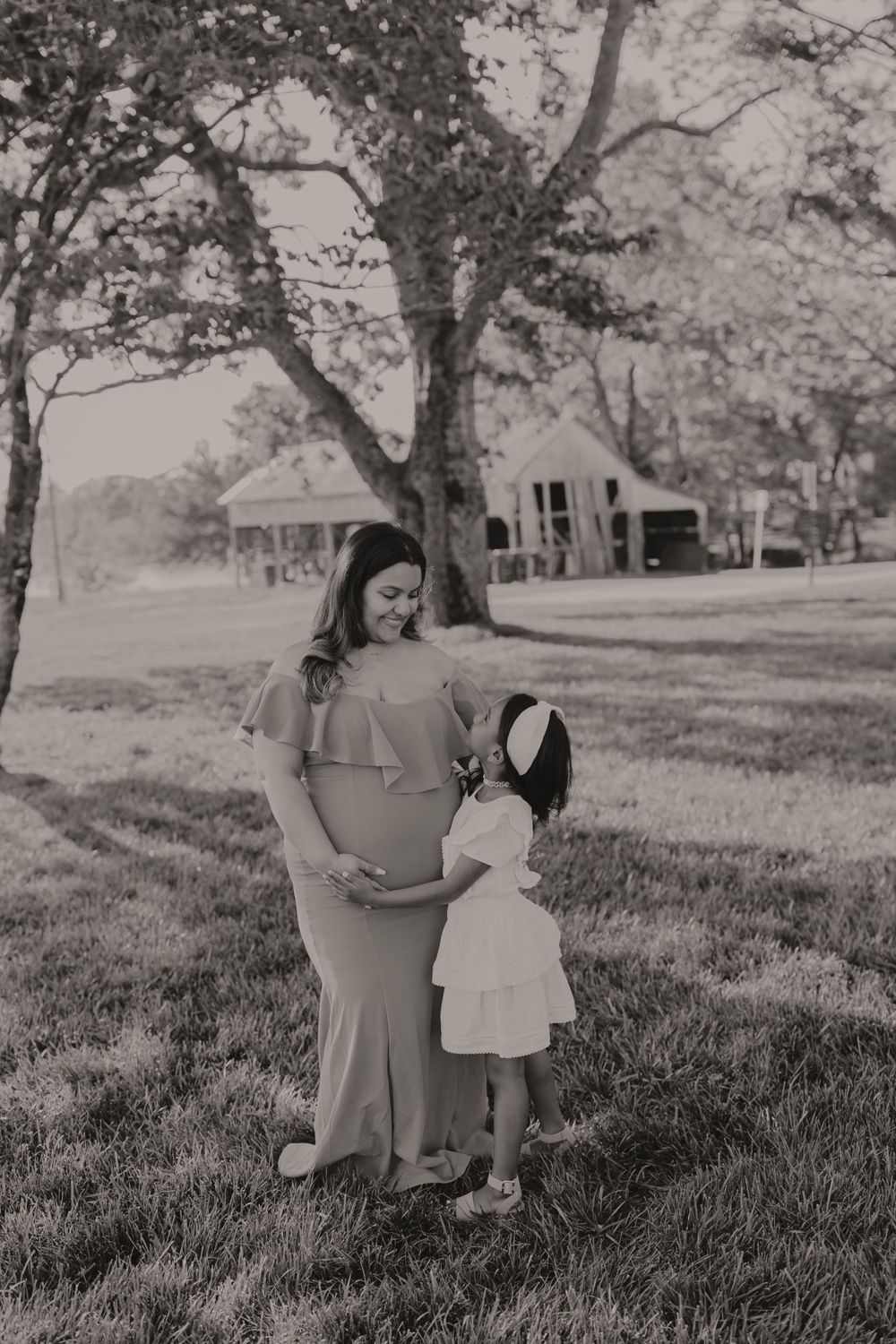 Vintage black and white photo of two people standing together under trees near rural buildings.