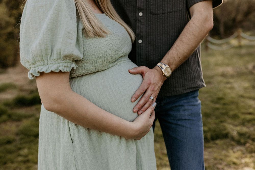 Close-up of couple's hands resting on pregnant belly in soft natural light.