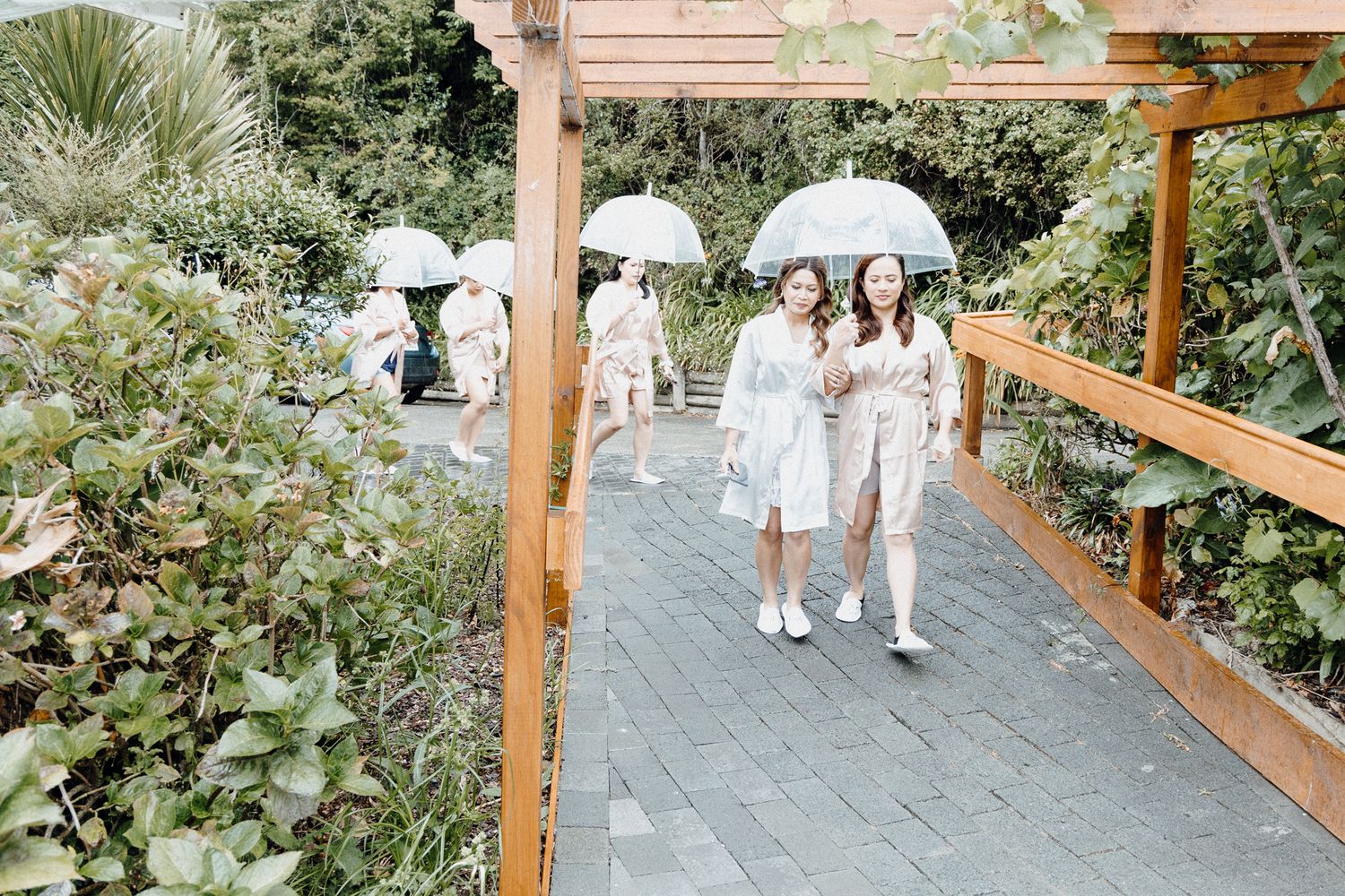 People walking on a garden path under white parasols captured by Apertured Media Auckland Wedding Photographer.