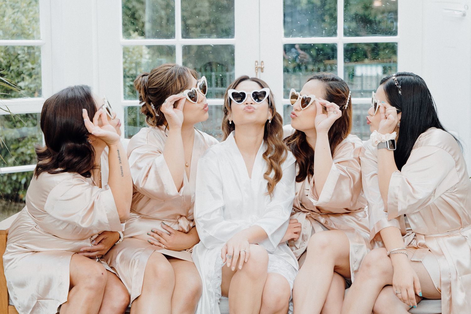 Women in matching silk robes and sunglasses laugh together captured by Apertured Media Auckland Wedding Photographer.