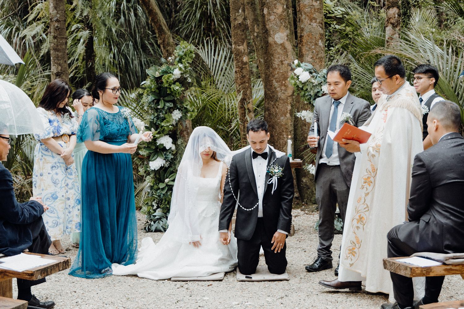 A catholic outdoor wedding ceremony takes place in a lush garden captured by Apertured Media Auckland Wedding Photographer.