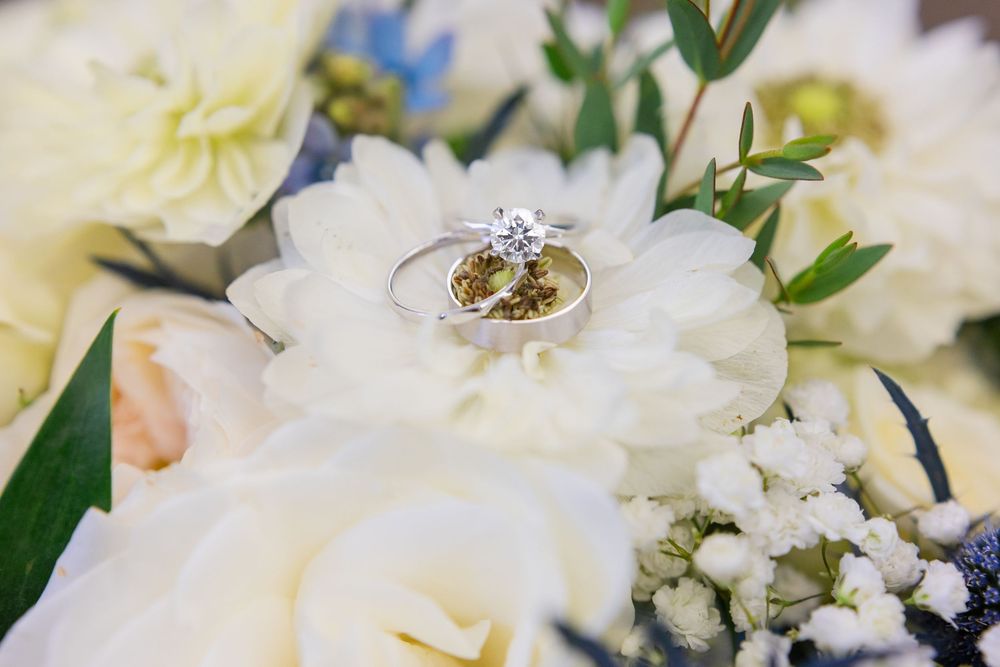 A brilliant diamond ring nestled in the center of a white flower surrounded by a delicate floral arrangement.