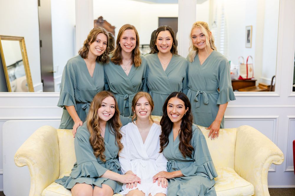 A group in matching sage green robes poses together on a yellow couch during a pre-wedding getting ready session.