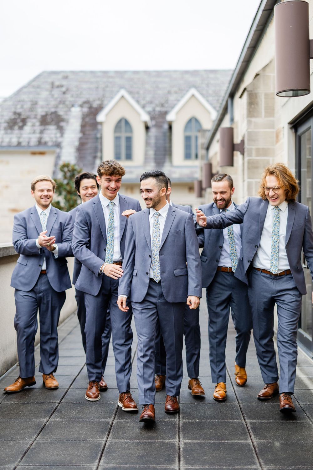Groomsmen in matching navy suits and brown shoes pose playfully for a series of candid shots.