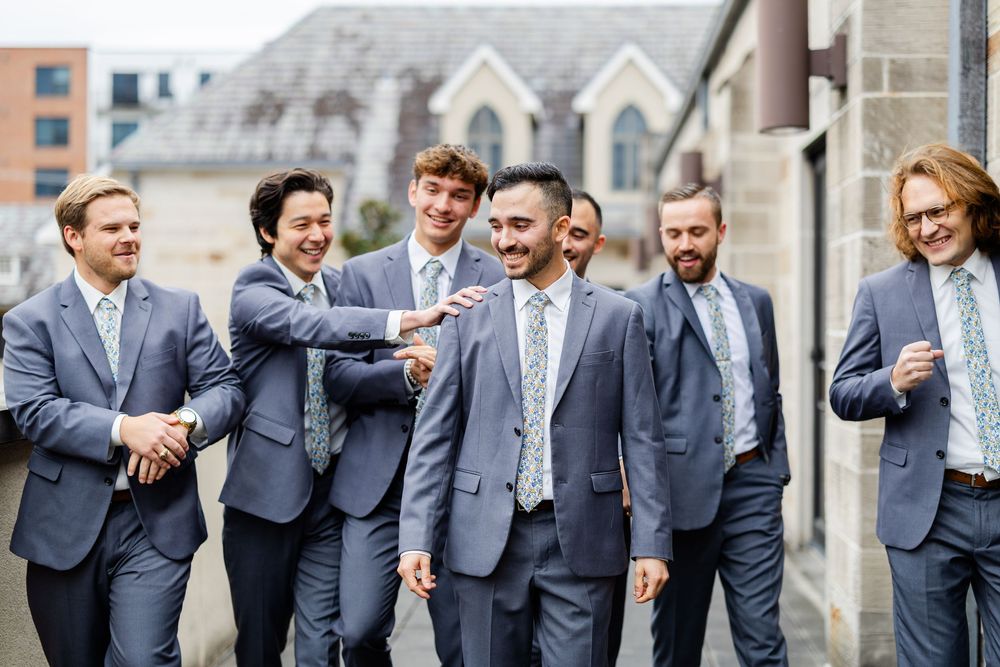 Group of groomsmen in matching navy suits sharing a lighthearted moment outdoors.
