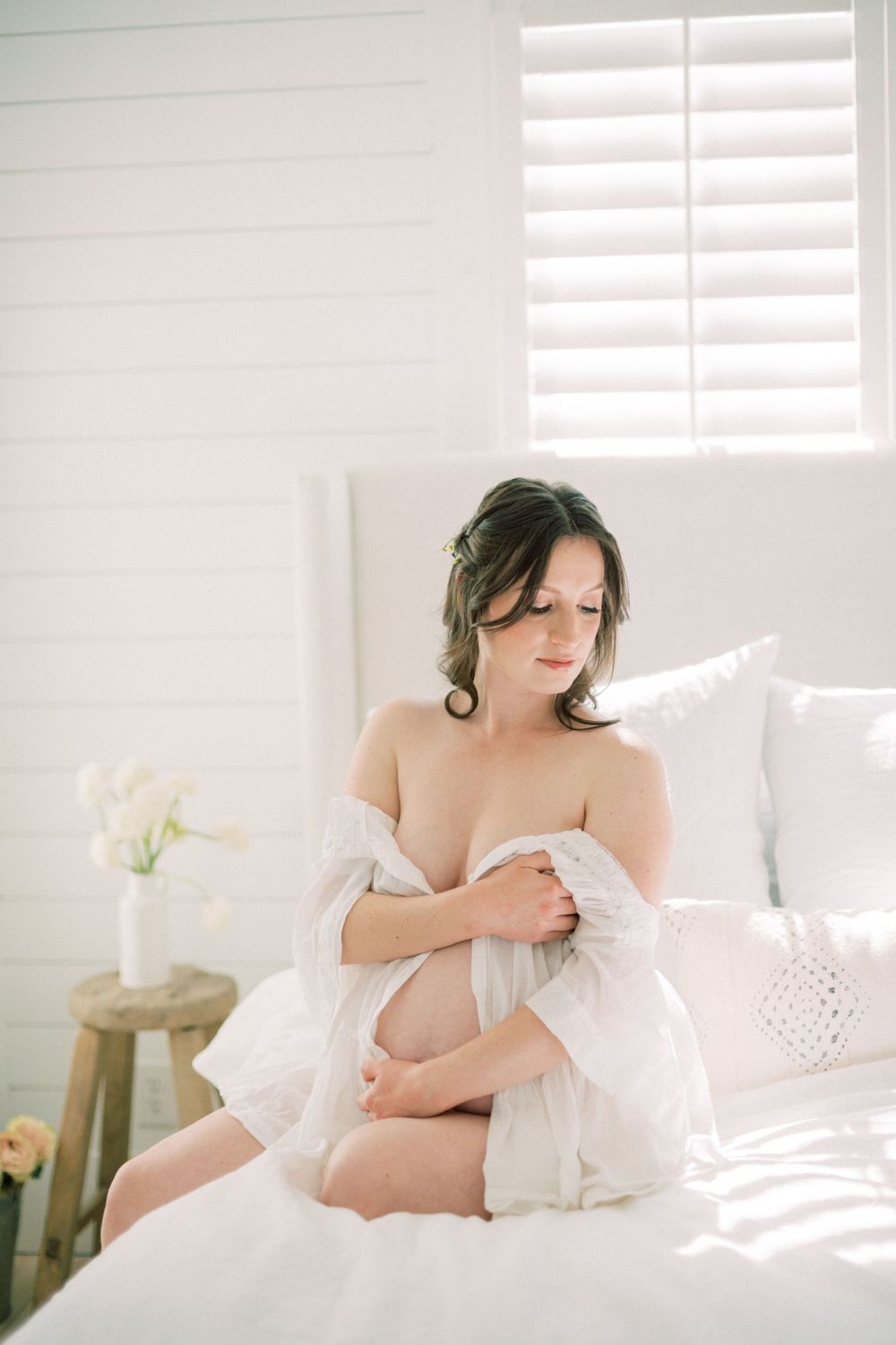 Dreamy boudoir scene with natural window light illuminating a white bedroom setting.