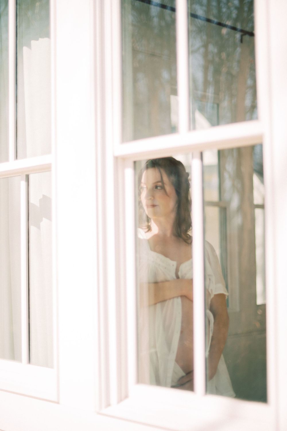 A dreamy window portrait shows a figure in white standing behind glass panes in soft, ethereal lighting.