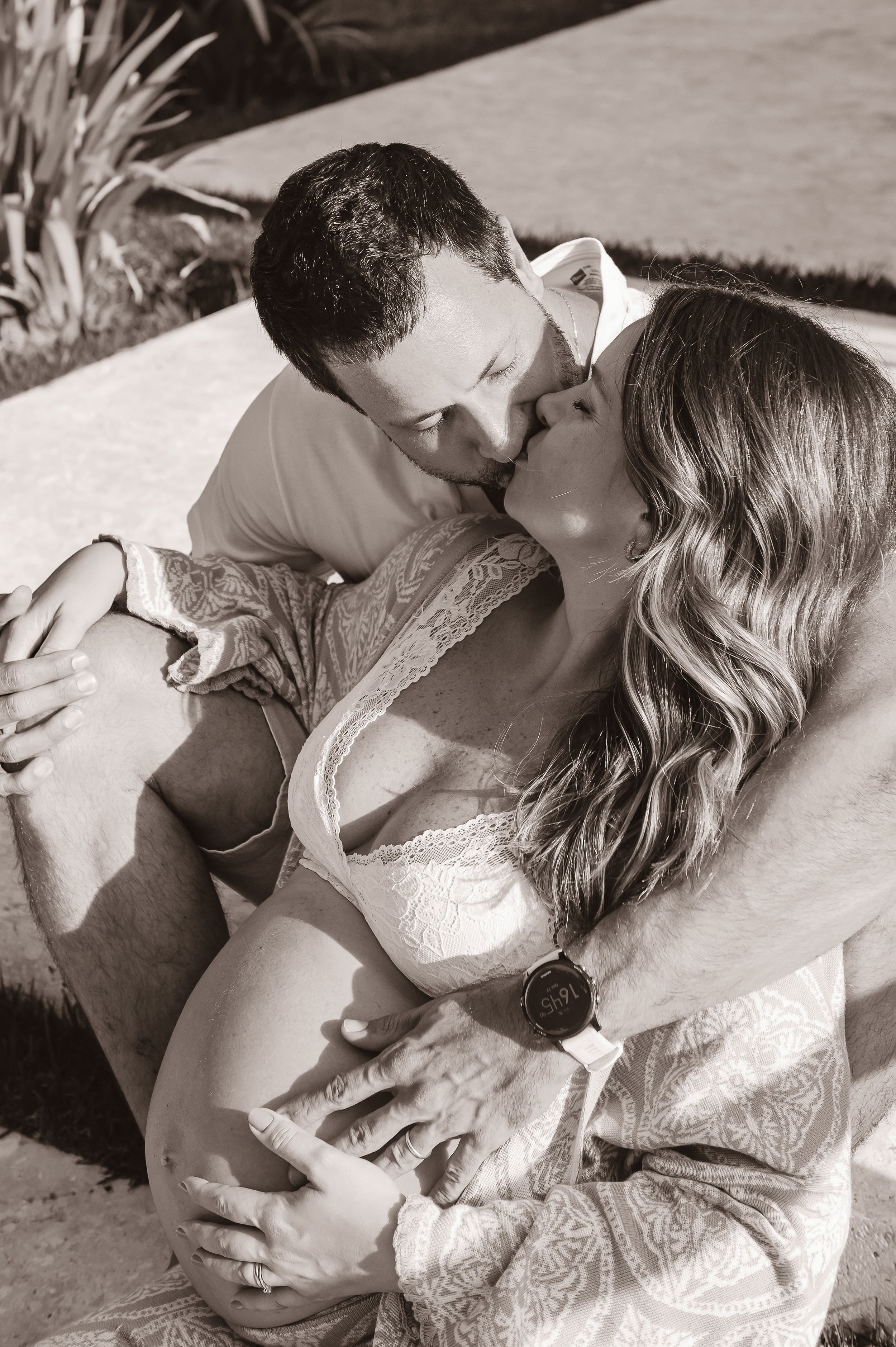 Romantic black and white portrait of a couple embracing and kissing tenderly on a patio lounge.