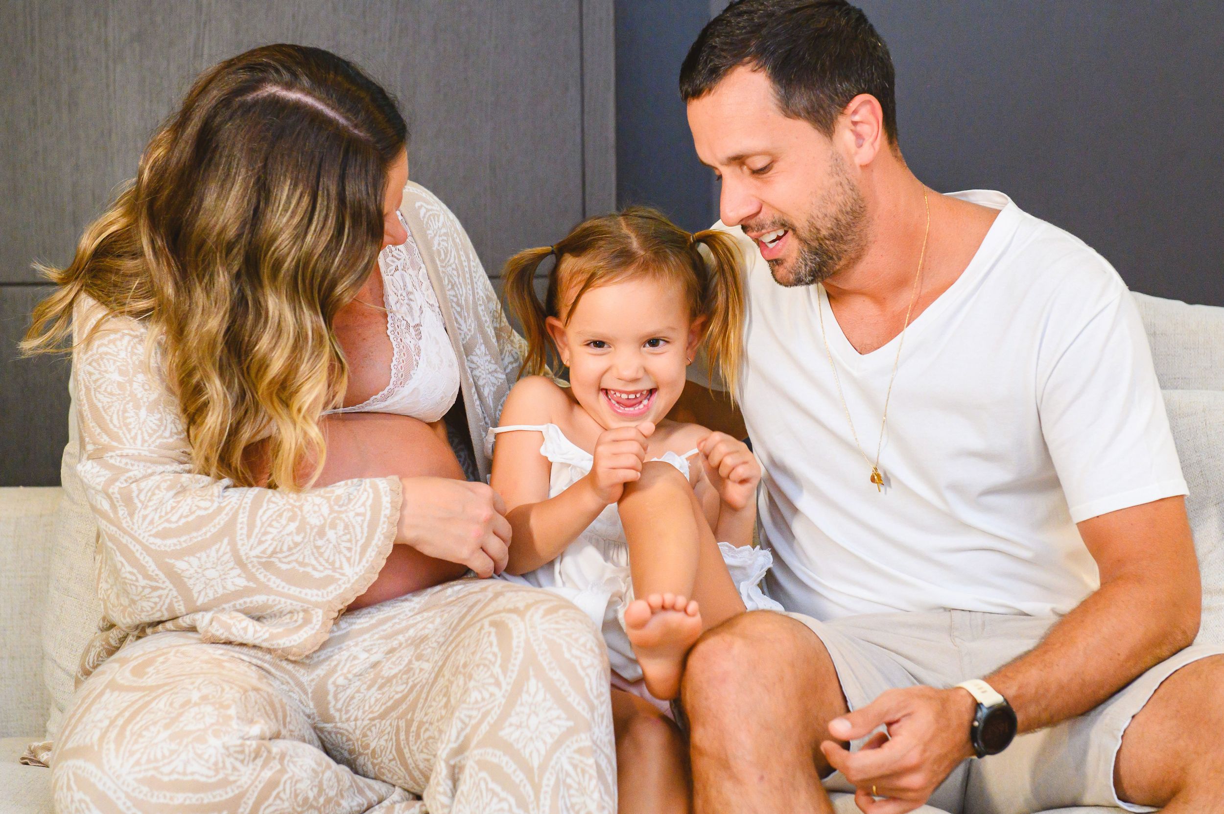 A family sits together on a couch sharing a joyful moment while dressed in casual white attire.