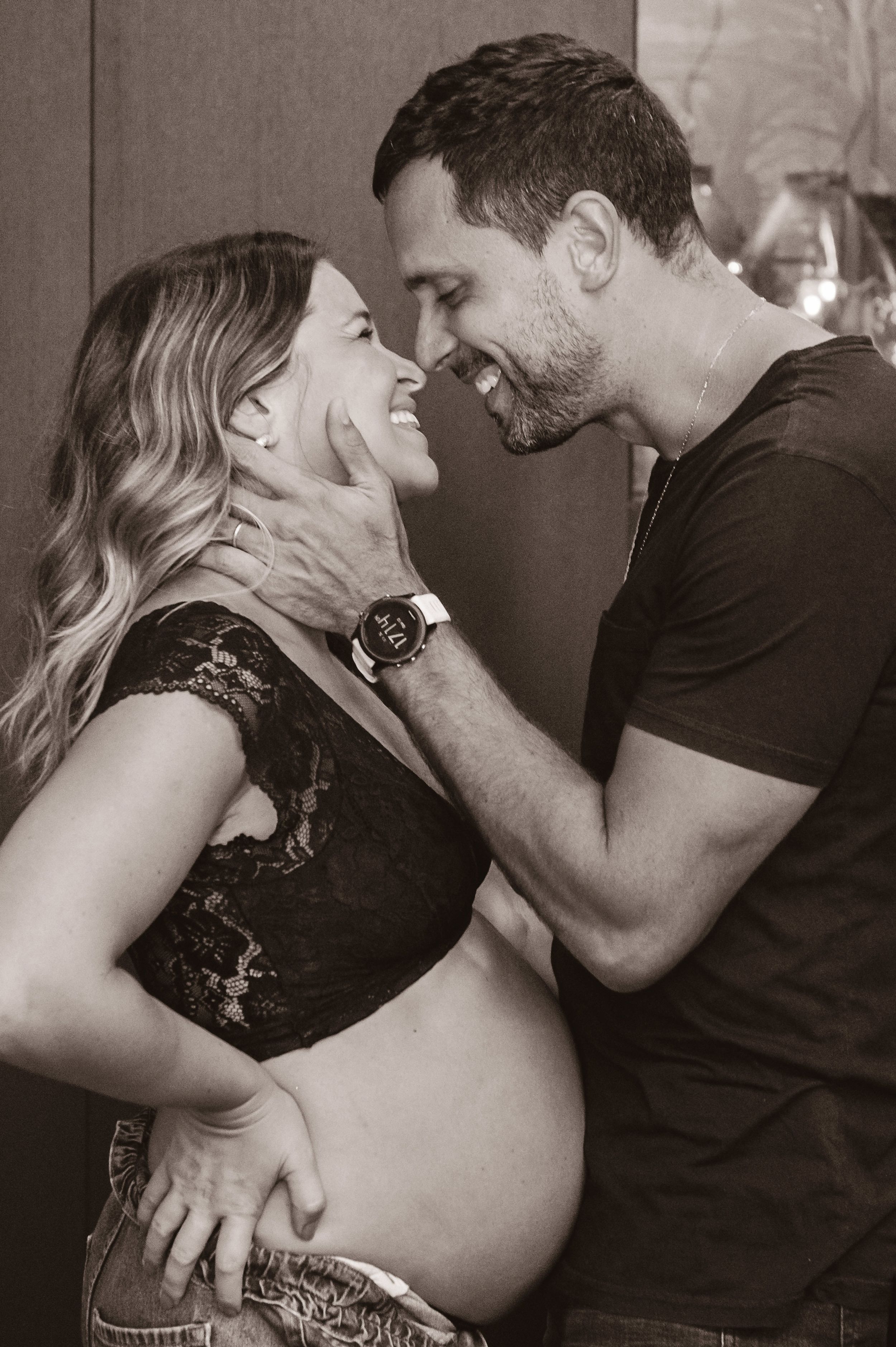Black and white photo of an intimate moment between a loving couple, with the woman displaying her pregnant belly.