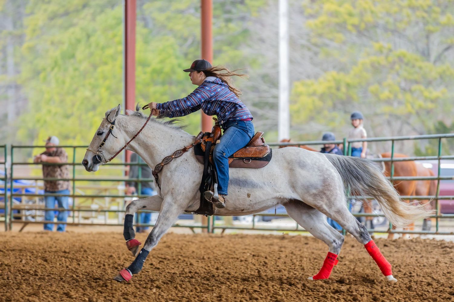 Rodeo rider races on white horse during competitive barrel racing event.