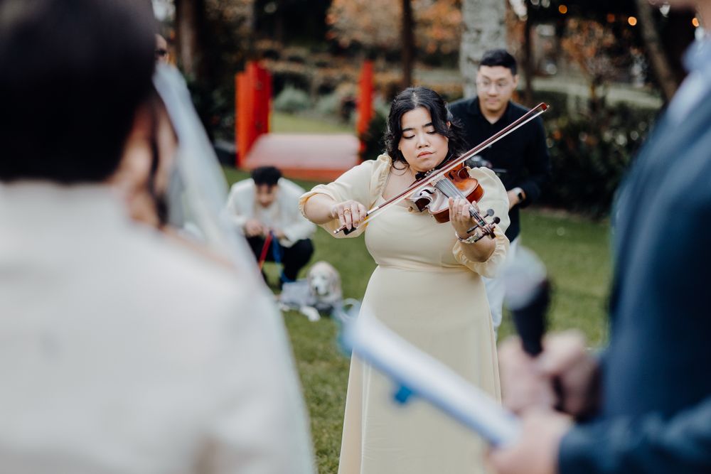 A musician performs with a violin during an outdoor wedding celebration.