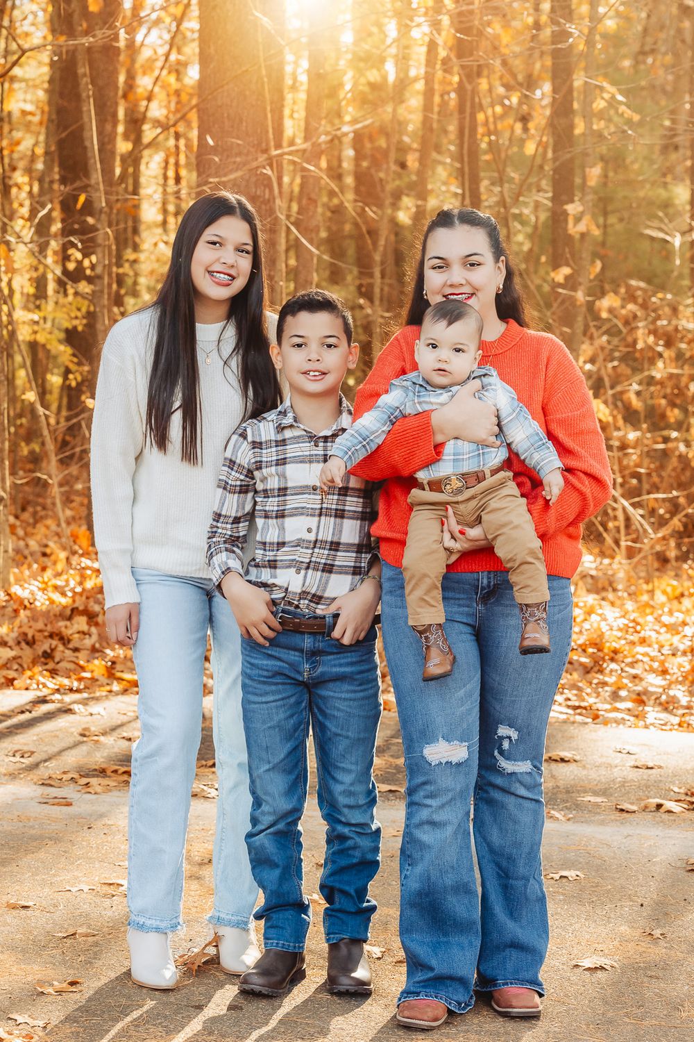 Family outdoor photo session with warm autumn colors and sunlit trees in background.