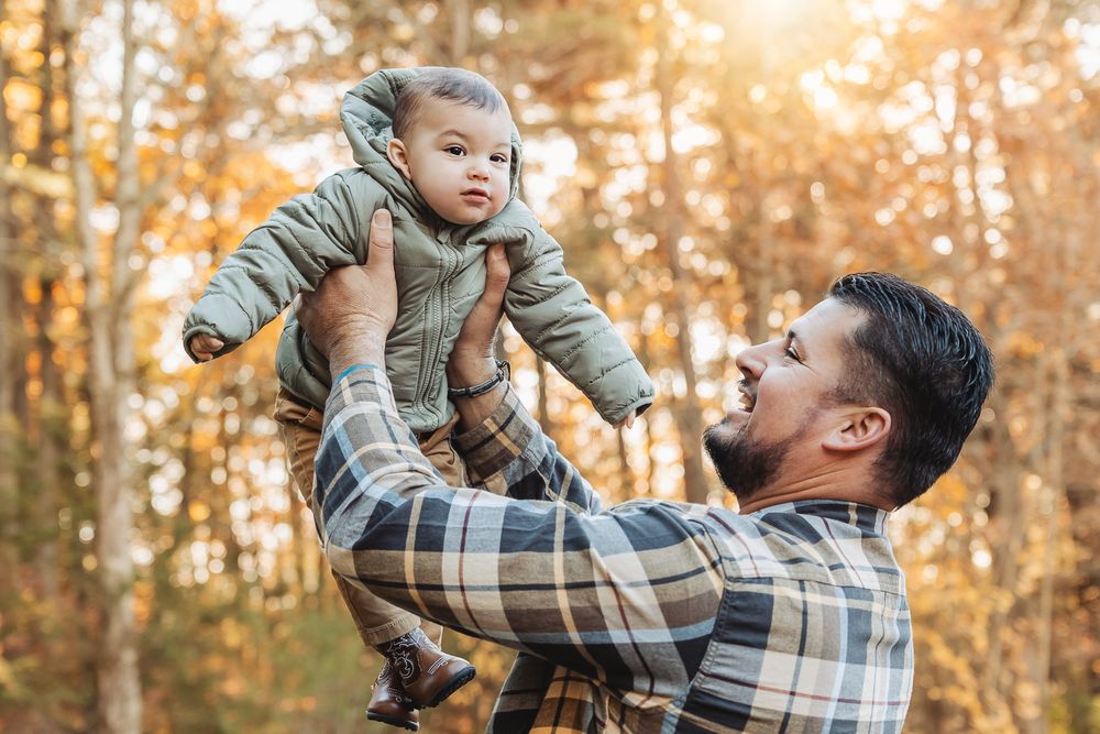 Playful moment between parent and baby during autumn outdoor photoshoot.