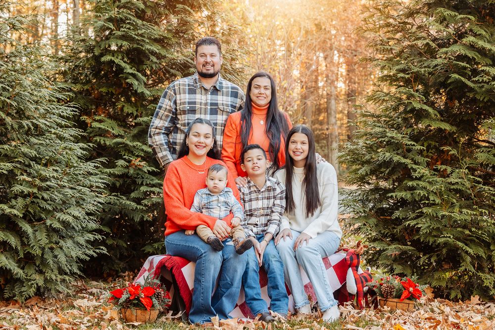 Holiday family portrait with evergreen trees and red decorations in autumn setting.