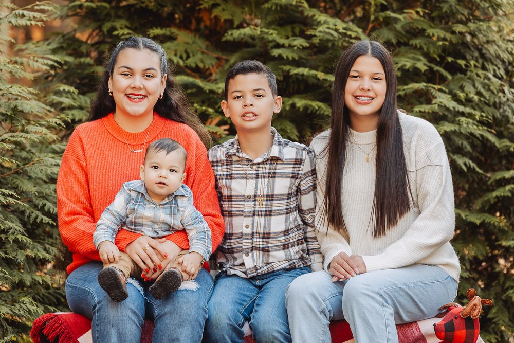 Casual outdoor family portrait on red bench with evergreen trees in background.