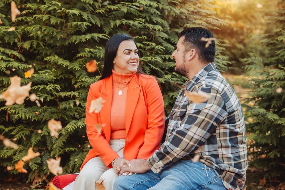 Couple sharing intimate moment on red bench against evergreen backdrop.