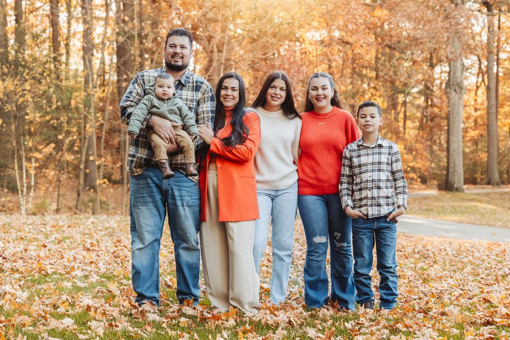 A family group poses together on a beautiful fall day with golden sunlight filtering through trees.