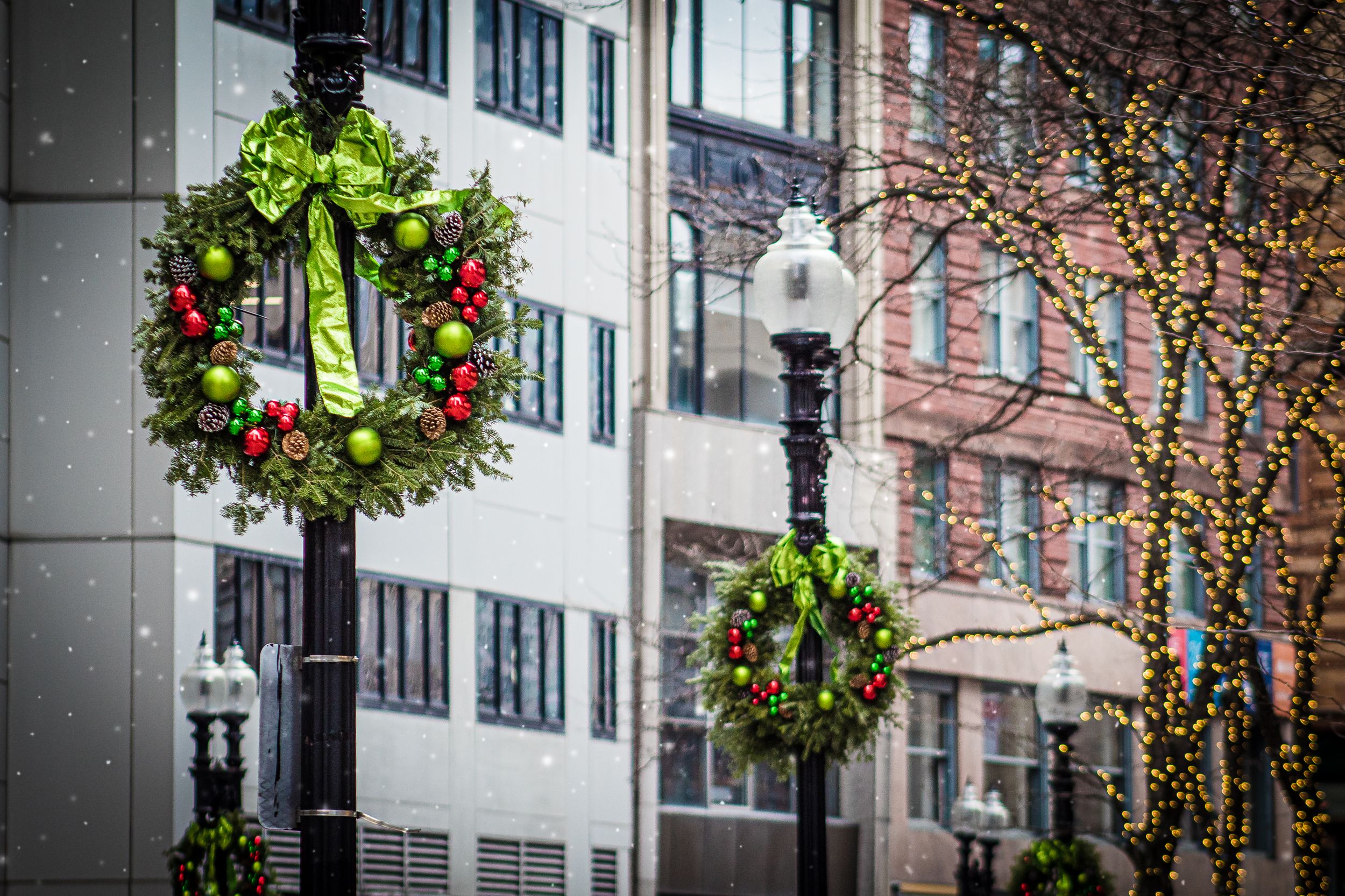 Holiday wreaths with red bows hang from lampposts on city street.