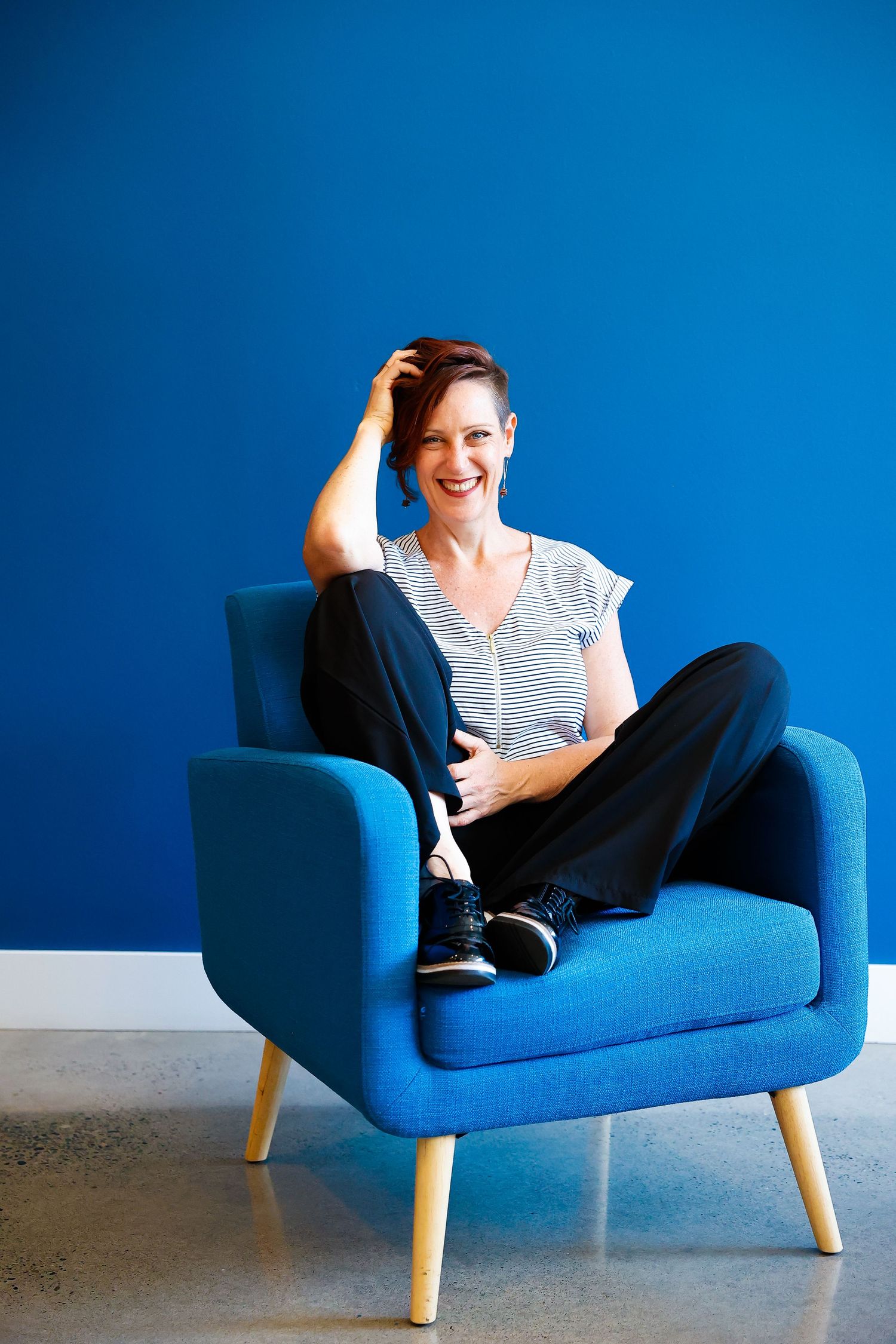 Relaxed casual portrait in bright blue armchair against vibrant blue wall.
