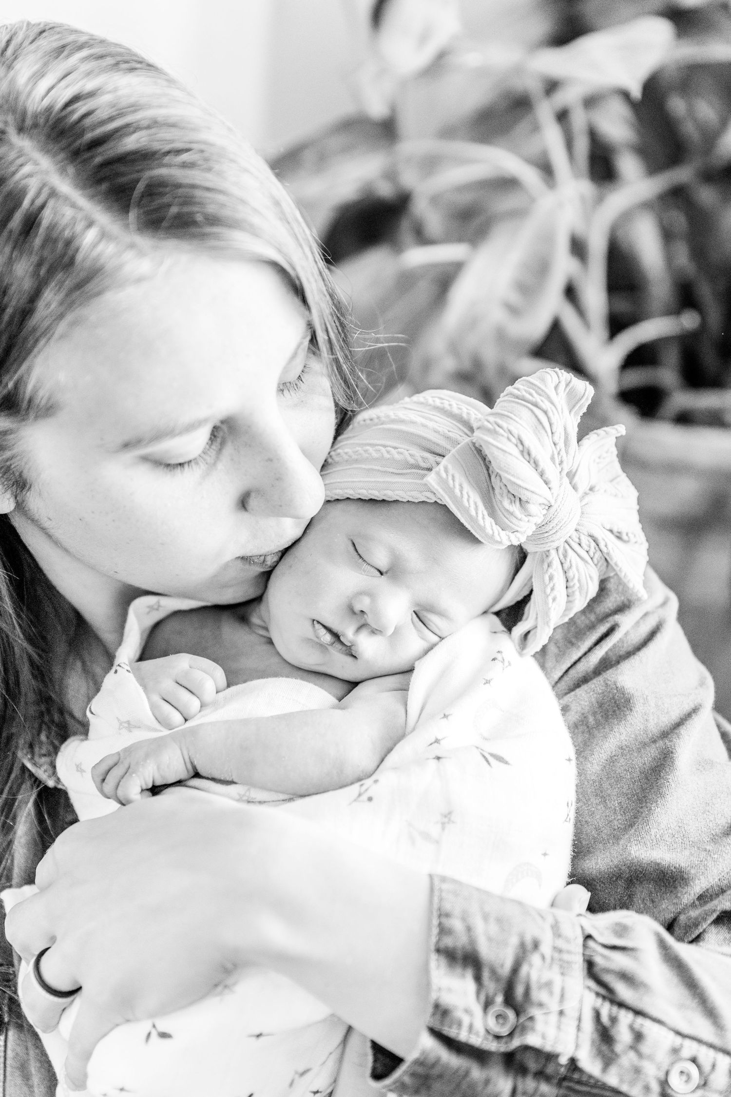 A tender black and white photo of a sleeping baby wearing a bow headband being cradled.