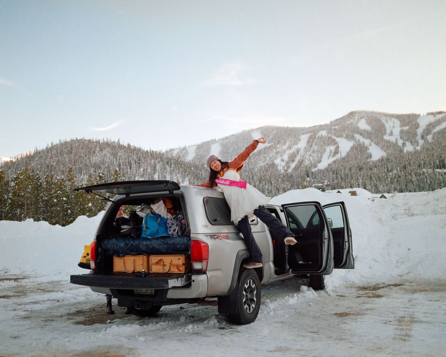 Person jumping excitedly next to an SUV in a snowy mountain landscape.