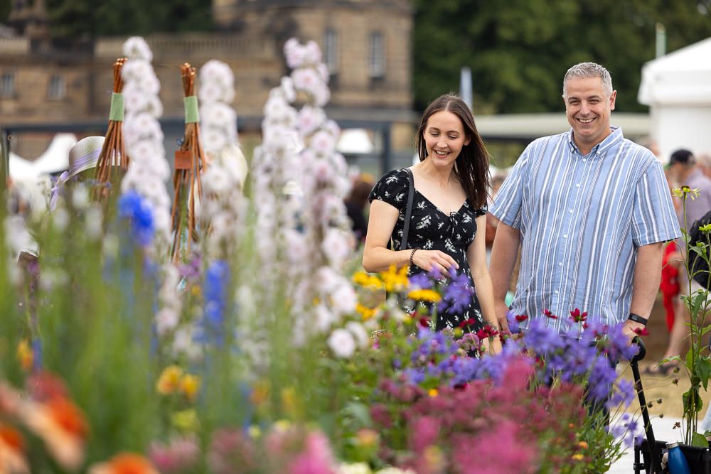 Couple walking together through a colorful garden path with delphinium and other summer flowers blooming.